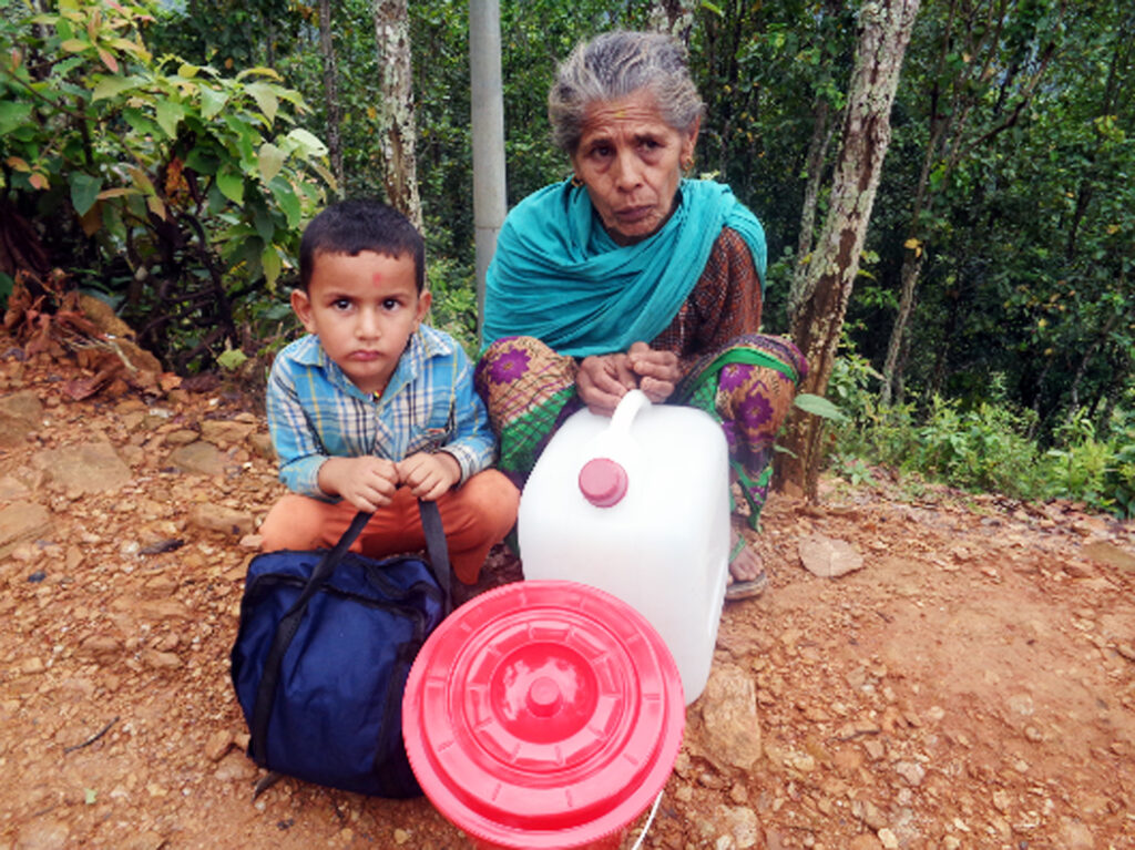 Indra and her grandson, Saurav, crouching on the ground in Chainpur holding hygiene kits they distribute to their community.