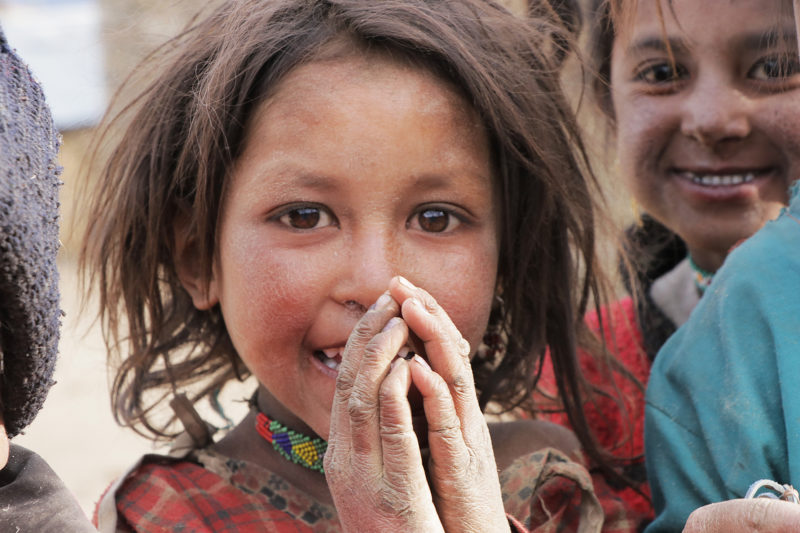 A little girl from the Chainpur community, looking into the camera smiling and covered in dirt