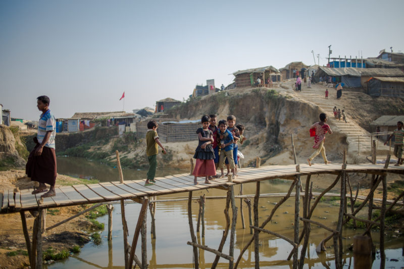 Rohingya refugee kid’s on top of a bridge over the river need low-lying homes in Bangladesh