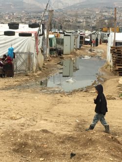 A boy walks through the muddy expanse of a settlement in Lebanon