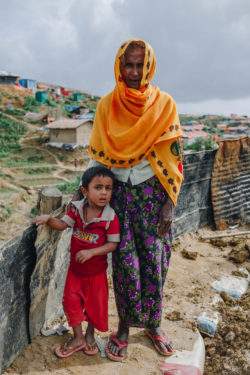 Amina and her grandson stand on muddy embankment in the Kutupalong refugee camp in Bangladesh