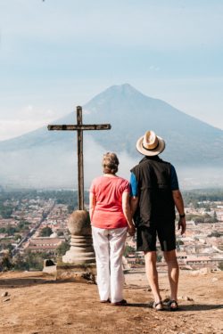 A man and a woman hold hands while looking toward a cross and volcano in Antigua, Guatemala